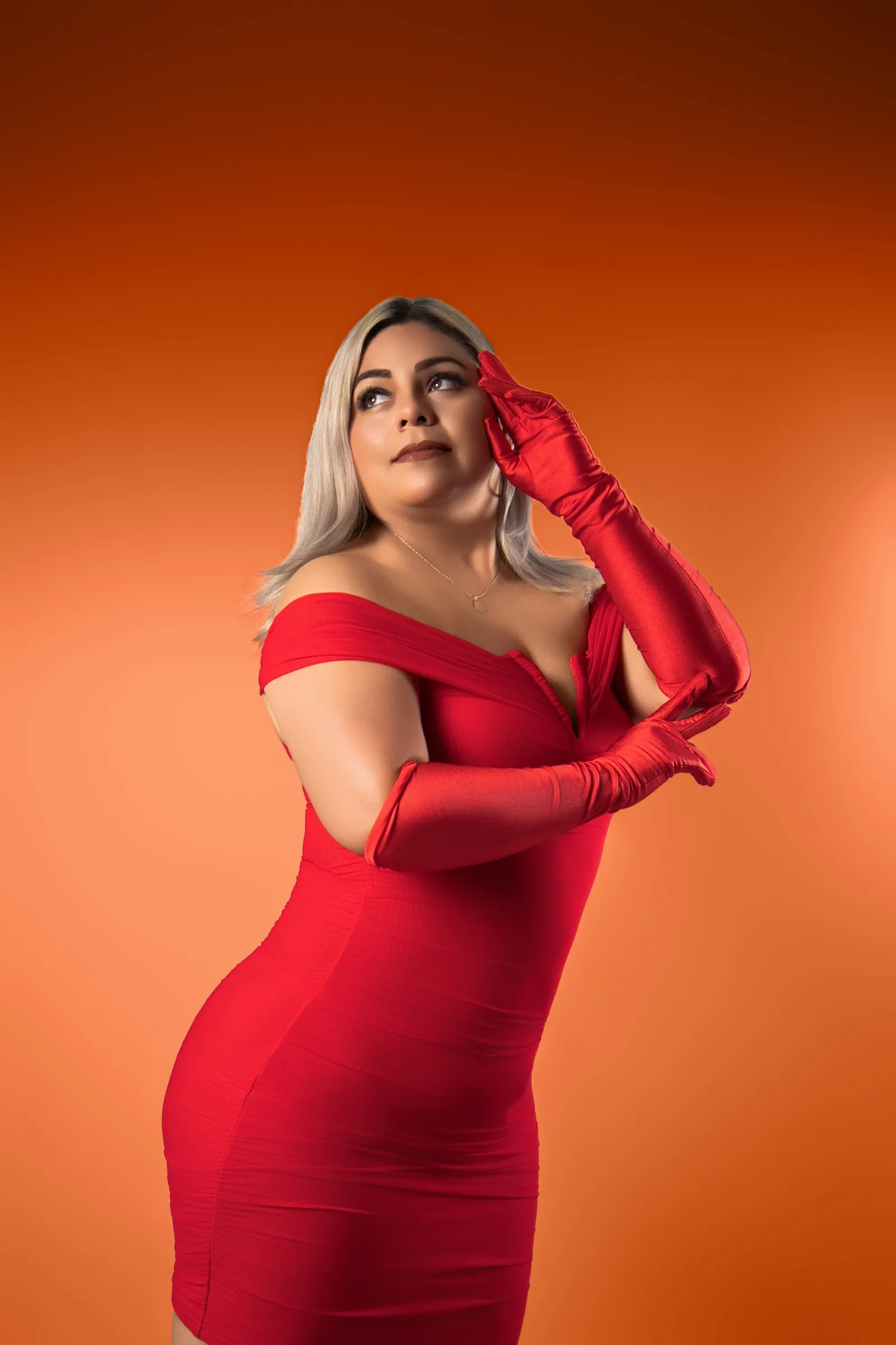 Adriana de pie con vestido rojo mirando hacia arriba, fondo naranja
