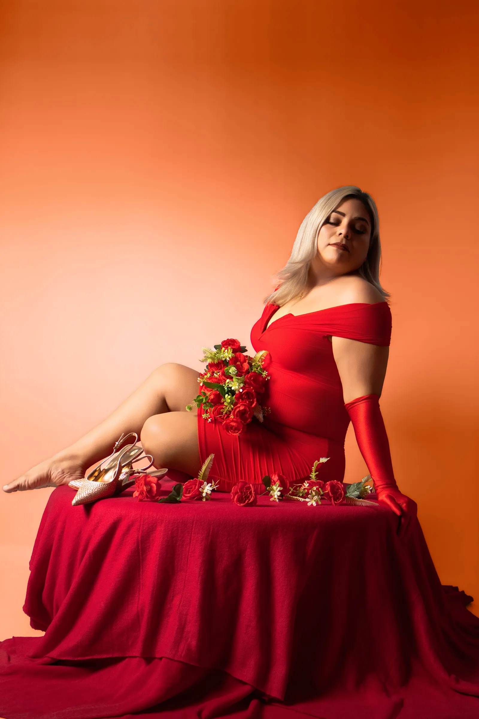 Adriana recostada sobre una tela roja con rosas y zapatillas doradas