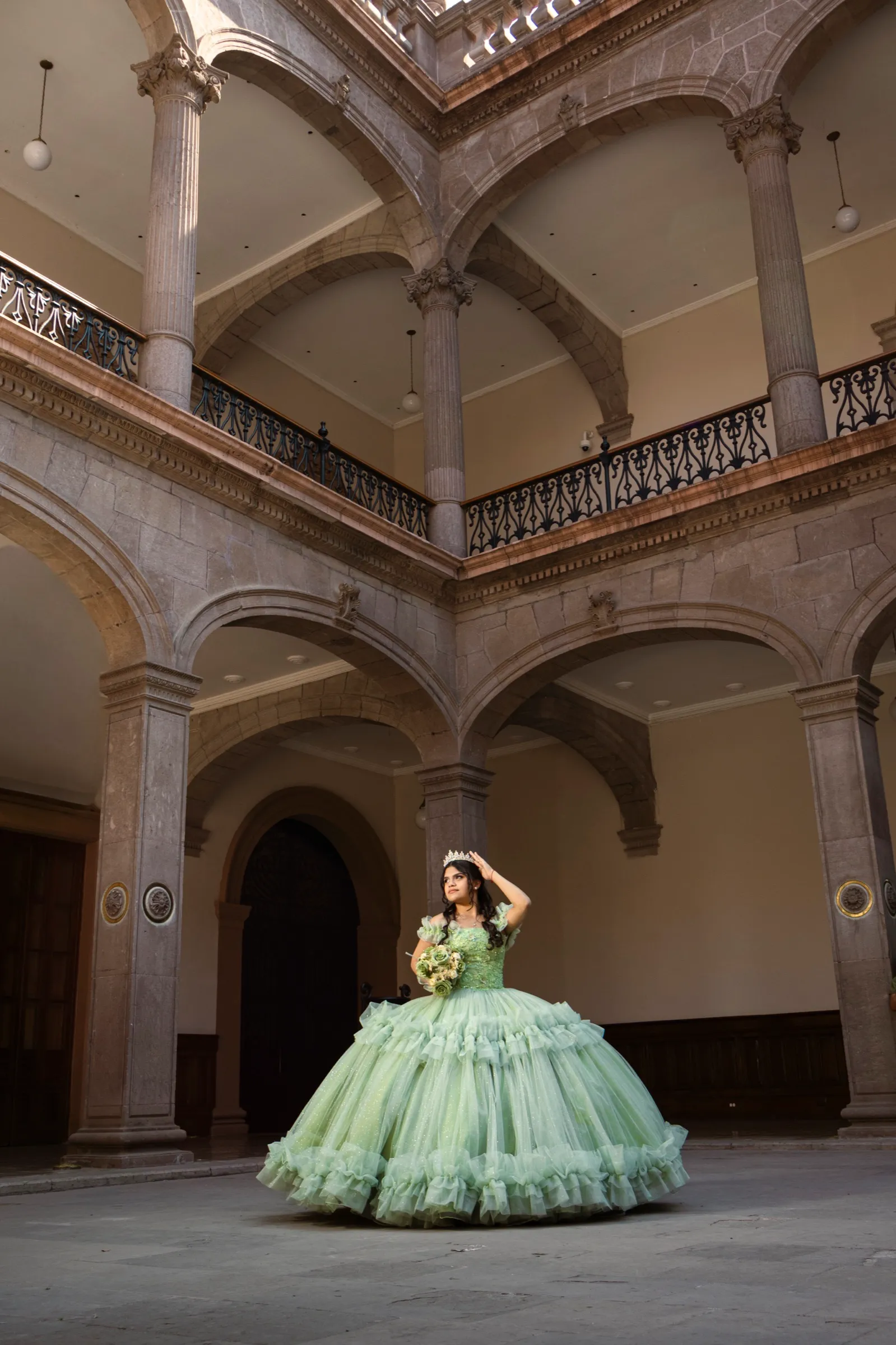 Camila con vestido verde en el patio de un edificio de cantera